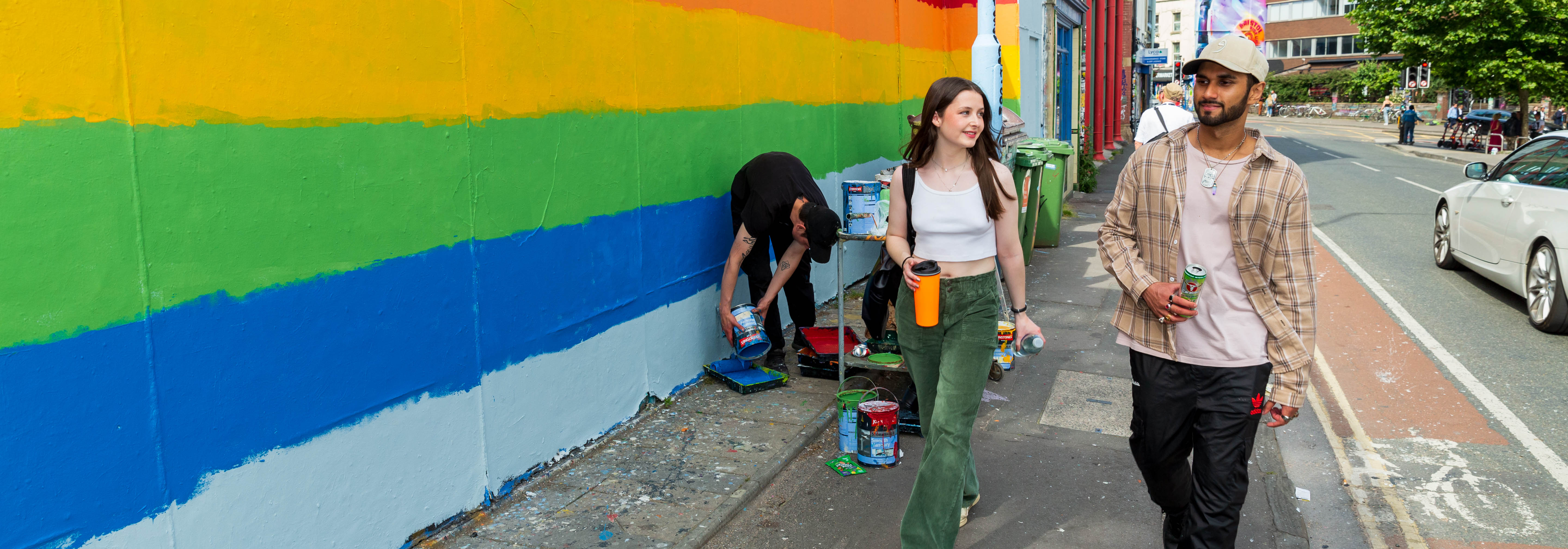 students walking down a city street in bristol, the wall to their left is painted with the pride rainbow